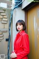 A woman in a red coat leaning against a wall.