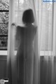 A woman standing in front of a window with sheer curtains.