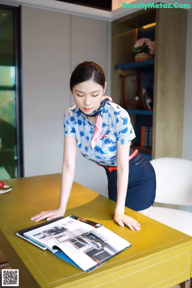 A woman in a blue shirt and skirt leaning over a yellow table.