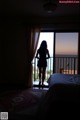 A woman standing in front of a window looking out at the ocean.